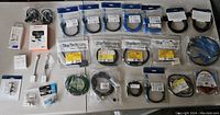 Lot of assorted cables and adapters laid out with visible packaging and labels showing various brands and types such as StarTech, Insignia, Monoprice, and more.