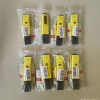 Eight yellow digital pH meters individually sealed in clear plastic packaging laid out in two rows of four on a flat surface.