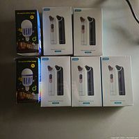 Five boxed blackhead remover devices in white and black, and two boxed mosquito killer lamp bulbs with yellow bug symbol on black packaging.