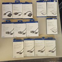 Photo showing 16 Insignia-branded cables and adapters in retail packaging arranged on a table. Includes HDMI to VGA adapters, Mini DP to VGA adapters, HDMI to DVI-D cables, and mini HDMI to HDMI cables.