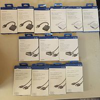 The photo shows 16 Insignia-branded boxed items arranged in three rows: four HDMI to VGA adapters, four Mini DisplayPort to VGA adapters, three HDMI to DVI-D cables (6ft), and four Mini HDMI to HDMI cables (4ft). Packaging is sealed with product image and specifications.