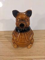 Front view of brown ceramic piggy bank shaped like a dog sitting on hind legs, showing detailed face, ears, and collar.