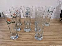 Nine Carlsberg beer glasses arranged on a wooden surface showing various logo prints.
