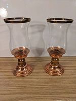 Pair of copper and glass hurricane candle holders on wooden surface against white background