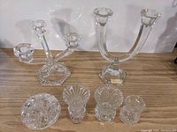 Photo showing two crystal candle holders at the back, three small crystal bud vases and one lidded container at the front on a wooden surface.