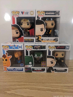 Front view of all five Funko Pop figures in their original packaging on a wooden surface, showing characters Wonder Woman, Sidney Crosby, Geoffrey as Superman, Batman, and Punisher with box numbers and logos.