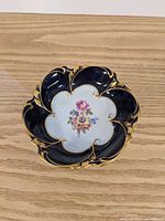 Top-down view showing floral bouquet center and scalloped navy blue and gold trimmed edge.