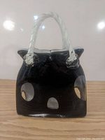 Front view of black glass handbag sculpture with white swirl glass handles, showing glossy surface with no chips