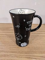Exterior side view of tall black ceramic Starbucks mug with white pumpkin faces and stars, showing Halloween theme and "Trick or Treat" text