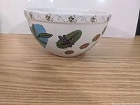 Side view of the largest bowl showing colorful insect designs of bees, dragonflies, and ladybugs on white ceramic.
