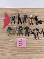 A top-down photo showing 9 Jurassic Park action figures and 7 accessories including weapons and a red glider wing on a wooden surface.