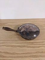 Side view of metal bed pan with wooden handle on wood surface.