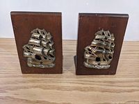 Front view showing two wood bookends with raised metal sailing ship decorations.