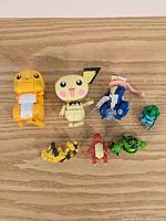 Seven Pokemon-themed building block figures displayed on a wooden surface, showing size and shape.