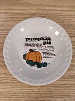 Top view of white ceramic plate with pumpkin pie recipe printed in center with text and pumpkin illustration.