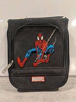 Front view of black disk holder case showing embroidered Spiderman design and Marvel logo patch on front pocket.
