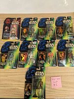 Ten Star Wars action figures still sealed on original backing cards arranged on a wooden surface.