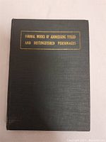 Front cover of an antique book with gold embossed title 'Formal Modes of Addressing Titled and Distinguished Personages' on a black cloth cover.