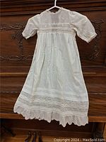 Full view of white antique christening gown hanging showing puffed long sleeves and lace detail at hem