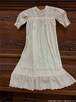 Full view of antique white christening gown showing long sleeves, lace neckline, pintucks on bodice, and embroidered scalloped hem.