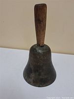 Front view of the antique hand bell with wooden handle against neutral background.