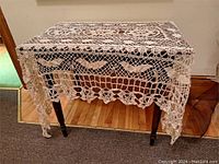 Full view of the antique crocheted tablecloth spread over a wooden table showing the full pattern and scalloped edges.