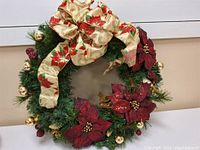 Front view of the Christmas wreath showing red poinsettias, gold baubles, pinecones and a large fabric bow with poinsettia pattern.