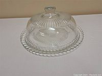 Clear glass cake plate with dome cover, showing scalloped edge and textured pattern on plate