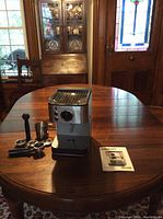 Full view of espresso maker with accessories arranged on table in a room with wooden furniture and stained glass window.
