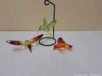 Three colorful plastic hummingbird figurines with one perched on a black metal stand.