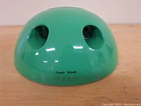 Green dome-shaped cat toy with two circular openings and power, sound buttons on side.