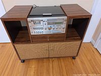 Full front view of mid-century modern wood cabinet featuring integrated stereo cassette and turntable system, showing the turntable cover and cane-front cabinet doors.