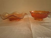 Two carnival glass bowls side by side on a cloth surface showing size and shape difference.