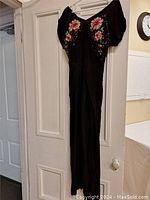 Full view of vintage black gown hanging showing overall shape and short sleeves.