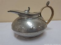 Side view of the rounded hammered pewter pitcher with hinged lid and handle showing overall shape and metallic finish.