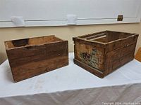 Photo showing two vintage wooden crates side by side on a table, highlighting size difference and general aged condition.