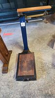 Full view of antique grain scale showing cast-iron frame, wooden platform, and brass balance beam.