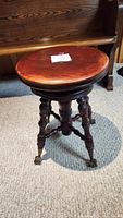 Full view of antique swivel piano stool showing turned legs and brass claw feet