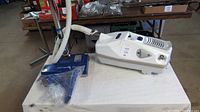 Miracle Mate Platinum vacuum cleaner shown assembled on a white table, visible flexible hose and blue cleaning head, showing good condition with no obvious damage or heavy wear.