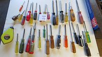 Top view of all screwdrivers and chalk line measuring tool displayed on white surface showing variety of handles and sizes.