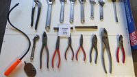 Photo showing laid out tools including open wrenches, pliers, a file, and a tool with an orange handle.