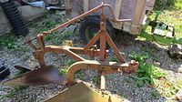 Front and side view showing two curved moldboards and metal frame with rust, intended to turn soil in farming.