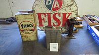 Veedol motor oil can, Edison car lamp battery and B/A Fisk round metal sign on a workbench