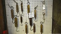 Overview photo displaying all 12 spring scales hanging against a pegboard background showing their size variation and condition.