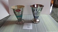 Two vintage tin measuring cups side by side on a table, showing full height and bases.