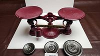 Refinished vintage cast iron balance weight scale painted in dark red with dual round pans and three included cast metal weights numbered 1, 2, and 3.