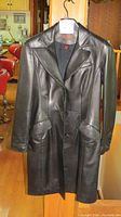 Front view of the long black leather coat showing button front, lapels, and flap pockets.