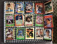 Full view of assorted baseball trading cards spread in a grid arrangement on a black-and-white checkered surface. Cards show various players and colorful borders.