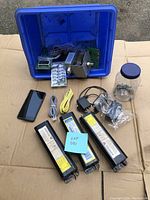 Overall lot layout showing the balance, electronic devices, cables, smartphone, blue bin with components, and jar with metal tips.