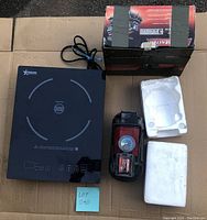 Photo of the tire compressor and induction cooktop on cardboard, showing front of induction cooktop with brand and controls visible, and tire compressor with pressure gauge and handle
